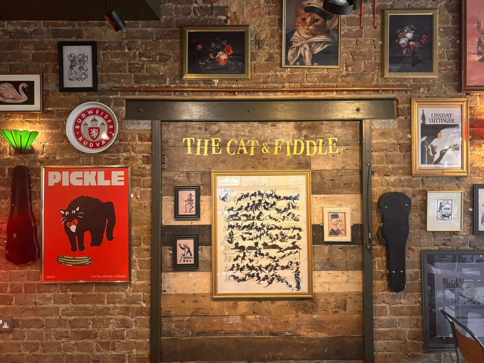 Brick feature wall with The Cat & Fiddle lettering, framed prints and lamps