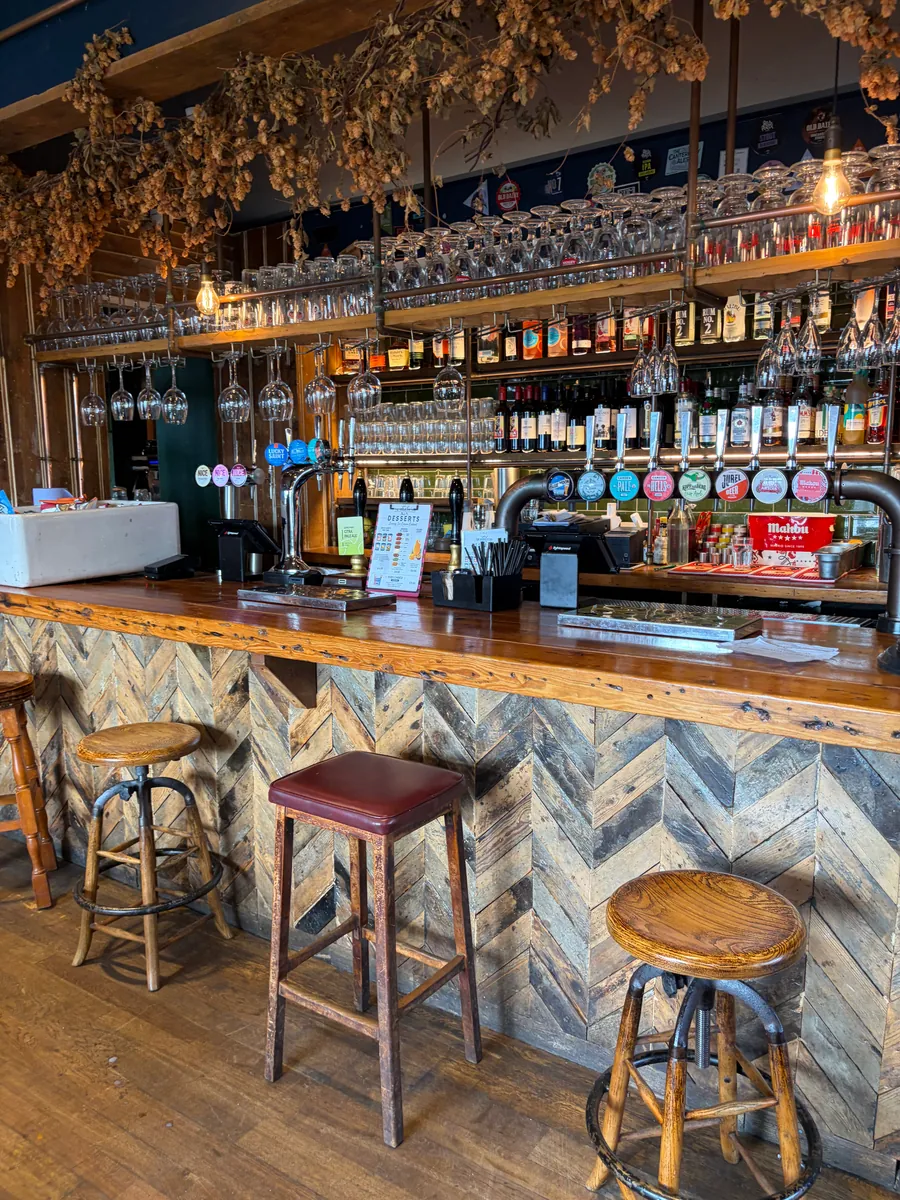 The bar counter with its blue herringbone front, bar stools and a wall of bottles