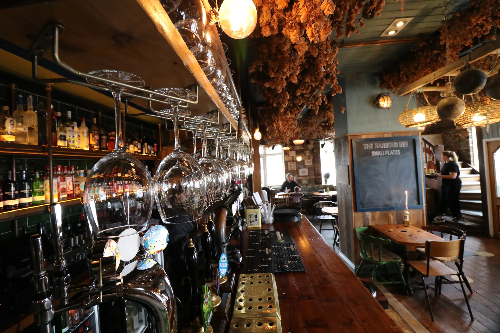 The Harbour Inn’s long bar, with dried flowers overhead, brass taps and a row of glasses catching the light