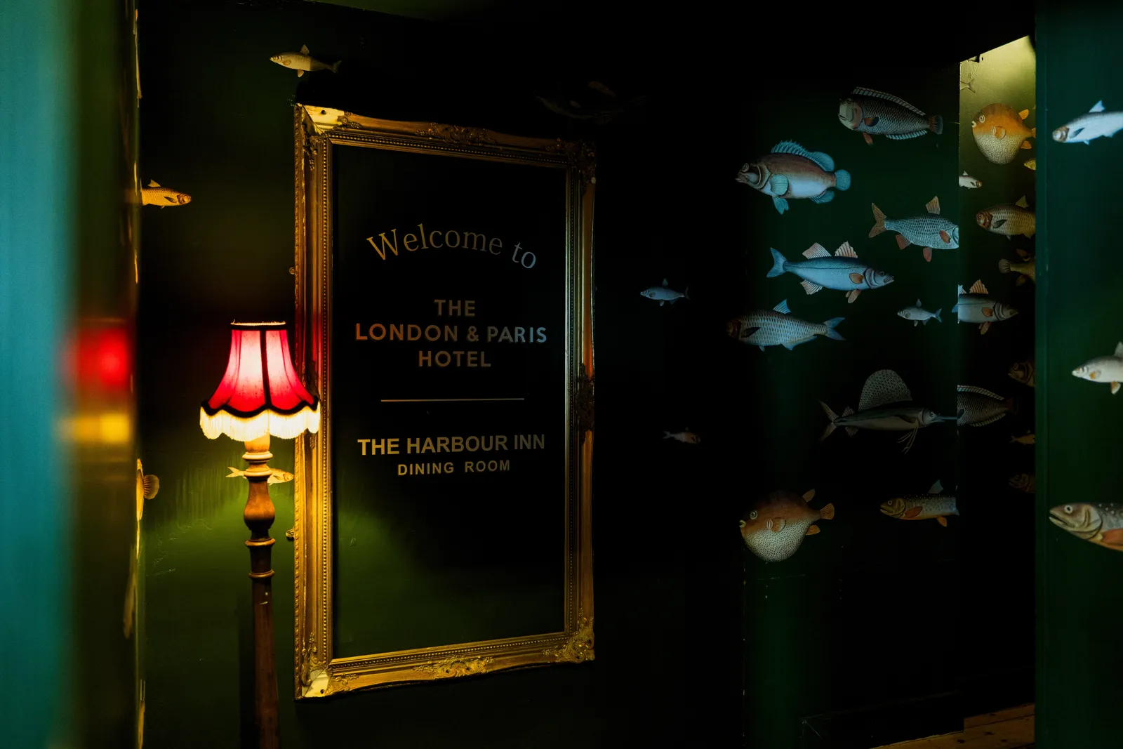A gilt 'Welcome to the London & Paris Hotel' sign beside a red lamp