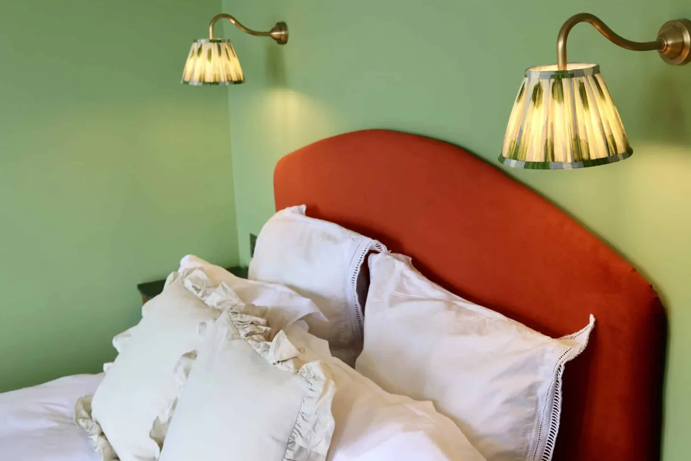 A superior room with a rust-red headboard and brass wall lamps on green walls