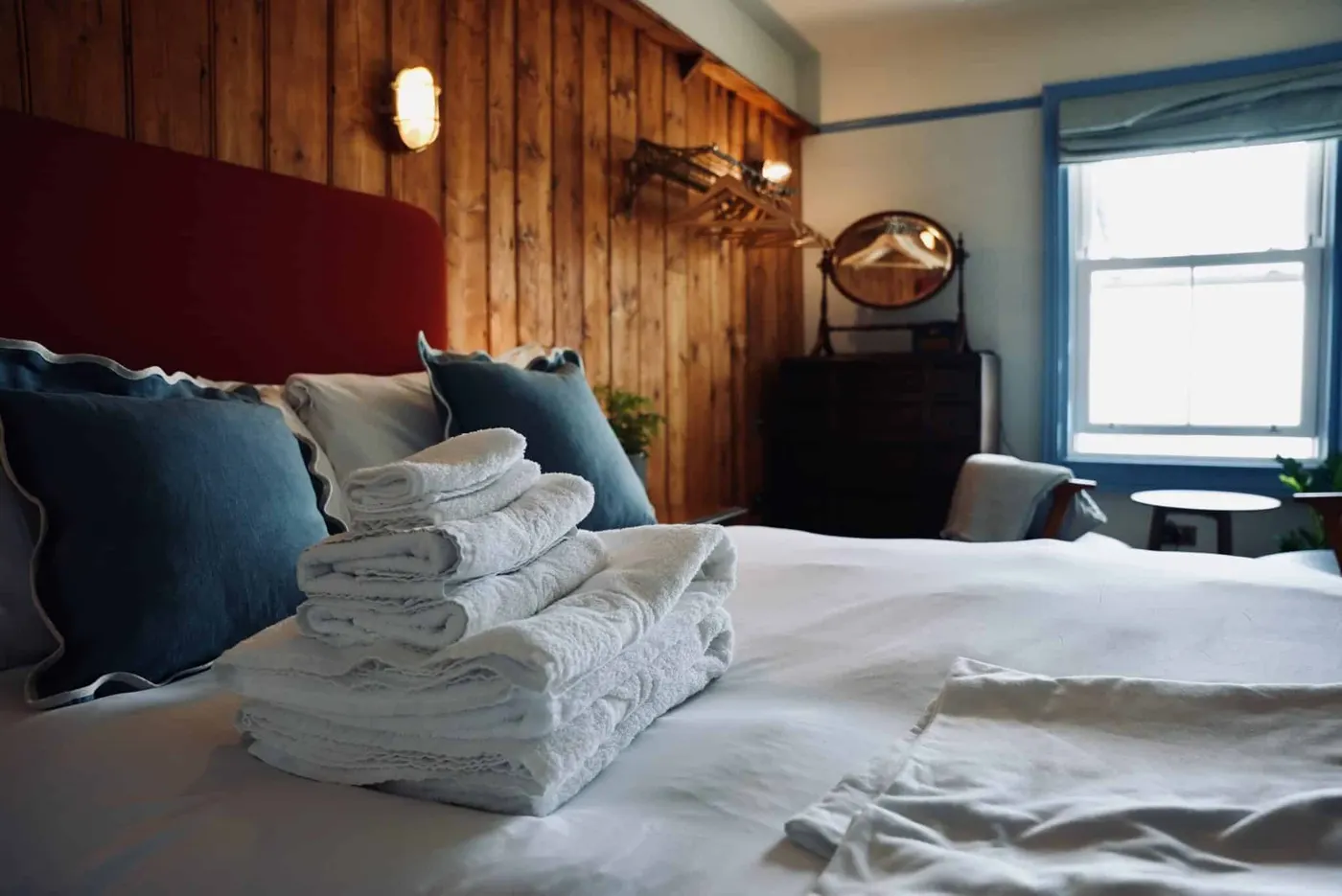 Room 8: a bed with a red headboard, a timber-clad wall and folded towels