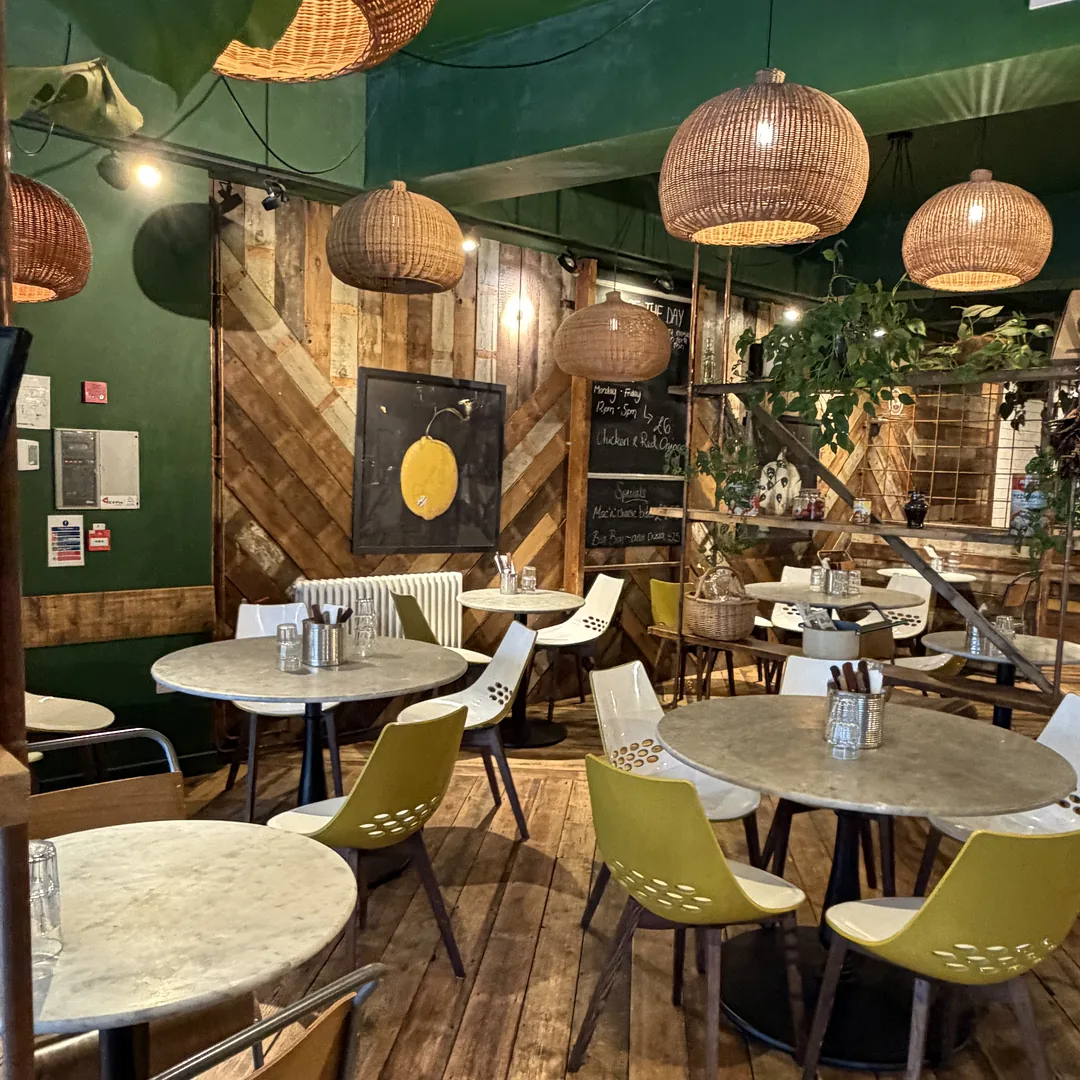 Inside Luben: woven pendant lamps over marble tables, olive-green chairs and a reclaimed-wood wall