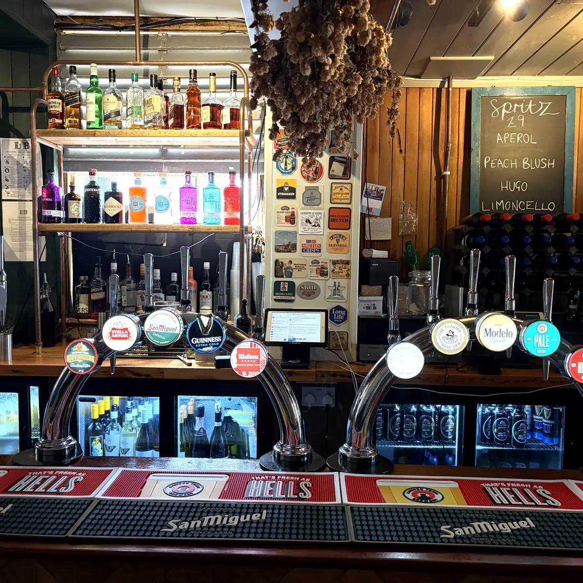 The bar at The Ship Inn, Sandgate: beer taps in front of a back bar of bottles and a chalkboard of drinks