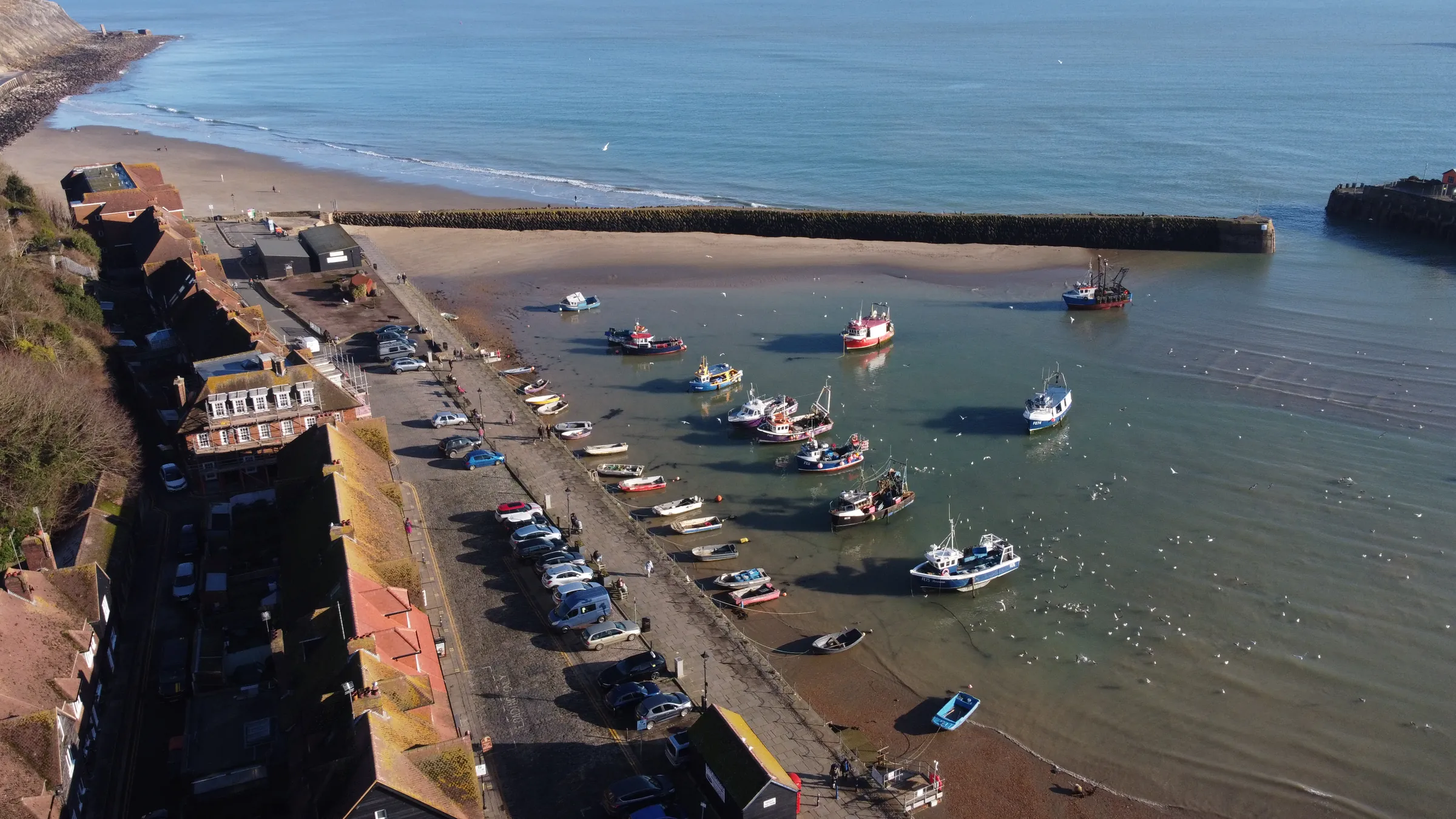 Aerial view of Folkestone’s outer harbour in bright sun: fishing boats on the water, the beach and the harbour wall