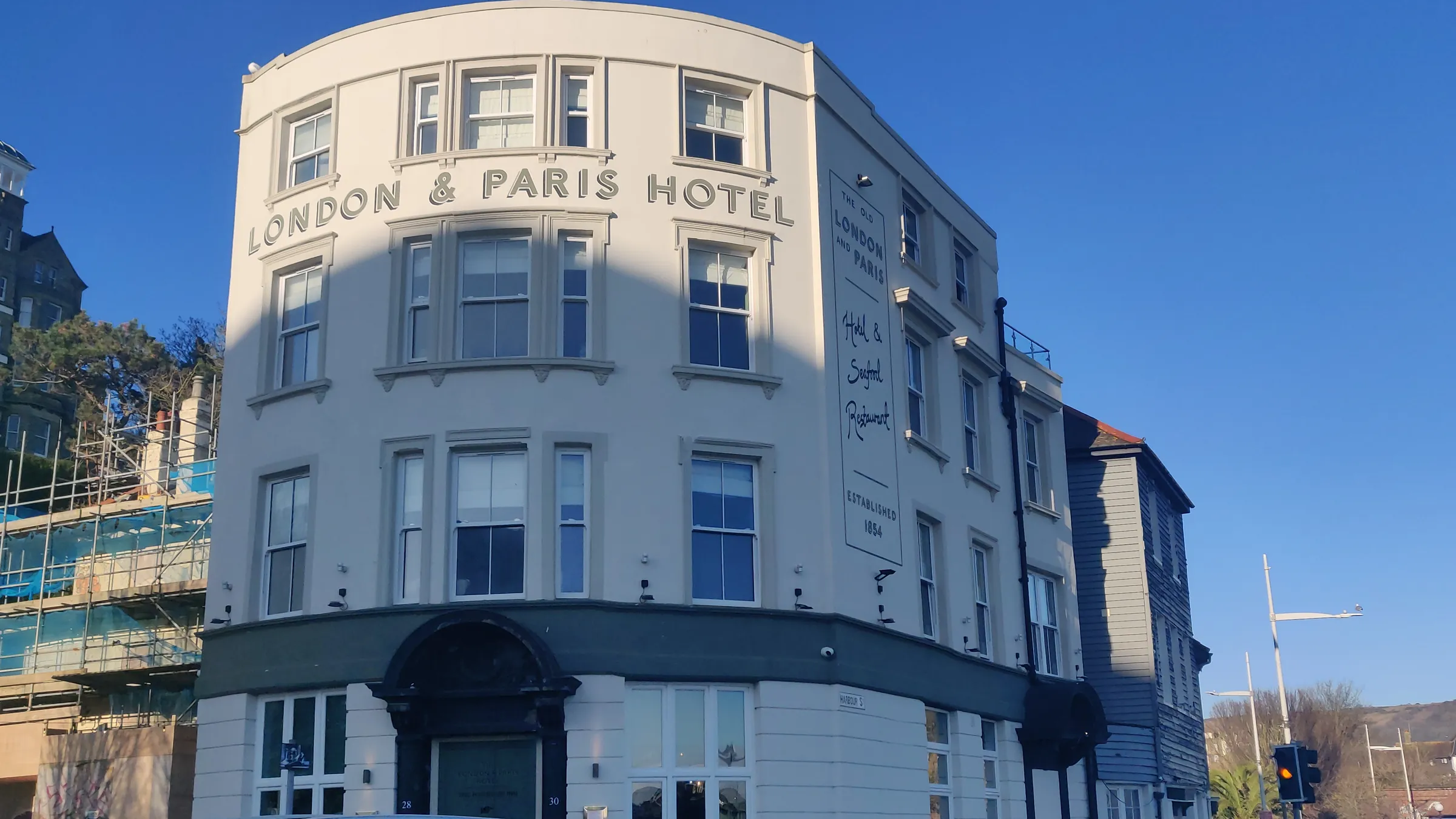 The curved white frontage of the London & Paris Hotel, its name in raised letters, under a deep blue sky